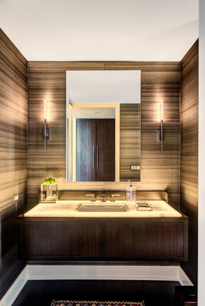 This is an example of a contemporary powder room in Detroit with flat-panel cabinets, brown cabinets, brown walls, a wall-mount sink, black floor and white benchtops.
