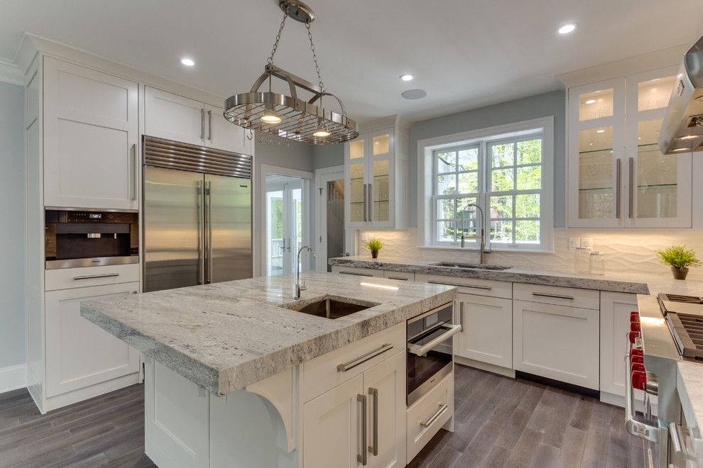 Inspiration for a large transitional l-shaped medium tone wood floor open concept kitchen remodel in DC Metro with a single-bowl sink, shaker cabinets, white cabinets, marble countertops, white backsplash, porcelain backsplash, stainless steel appliances and an island