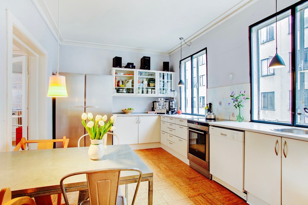 Inspiration for a mid-sized contemporary l-shaped eat-in kitchen in Copenhagen with a drop-in sink, flat-panel cabinets, white cabinets, laminate benchtops, multi-coloured splashback, porcelain splashback, stainless steel appliances, cork floors and no island.