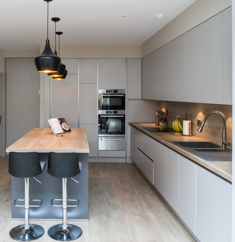 Mid-sized contemporary l-shaped eat-in kitchen in Other with an integrated sink, flat-panel cabinets, beige cabinets, laminate benchtops, beige splashback, timber splashback, stainless steel appliances, light hardwood floors and with island.