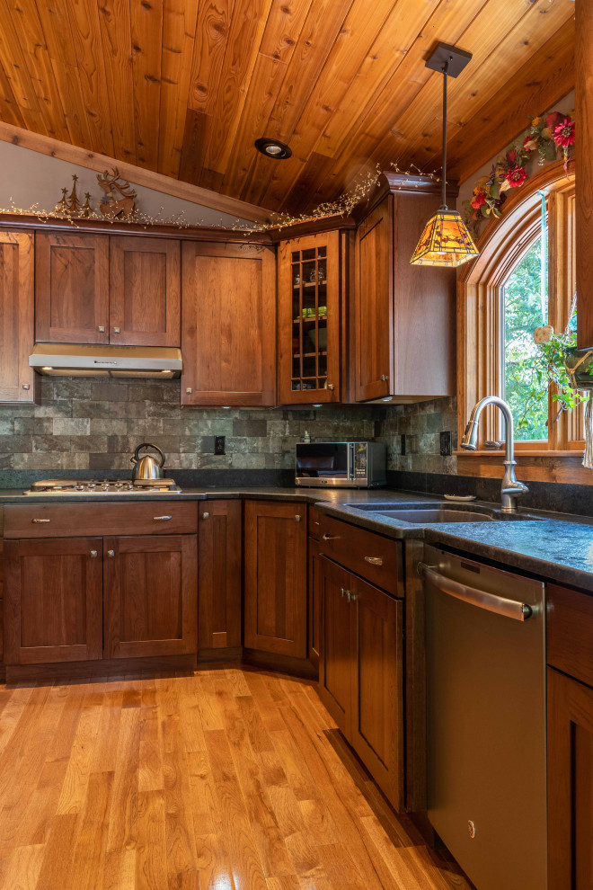 Inspiration for a mid-sized country l-shaped open plan kitchen in Burlington with an undermount sink, recessed-panel cabinets, medium wood cabinets, grey splashback, stainless steel appliances, medium hardwood floors, with island, brown floor, black benchtop and wood.