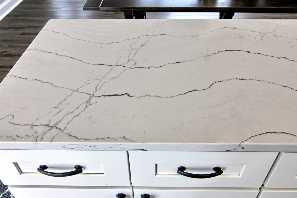 Inspiration for a mid-sized transitional l-shaped vinyl floor eat-in kitchen remodel with a farmhouse sink, shaker cabinets, white cabinets, quartz countertops, white backsplash, stone tile backsplash, stainless steel appliances and an island