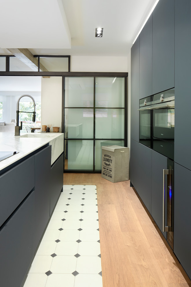 This is an example of a large industrial galley open plan kitchen in Other with a drop-in sink, open cabinets, black cabinets, marble benchtops, white splashback, brick splashback, stainless steel appliances, porcelain floors, with island and white floor.