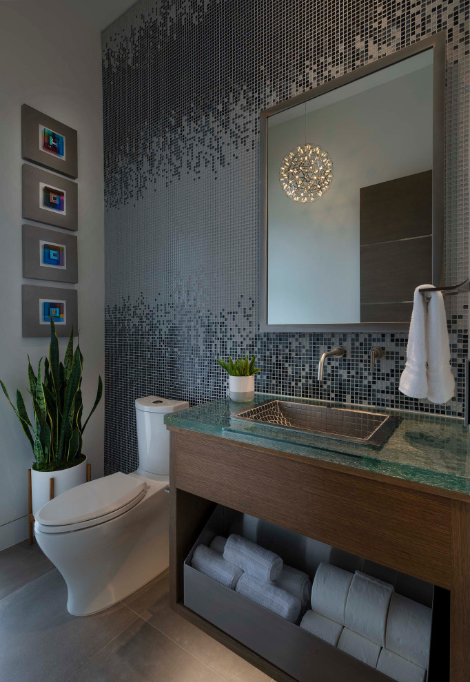 Photo of a mid-sized contemporary 3/4 bathroom in Dallas with open cabinets, medium wood cabinets, a one-piece toilet, gray tile, glass tile, white walls, porcelain floors, a drop-in sink, glass benchtops, grey floor, green benchtops, an enclosed toilet, a single vanity and a floating vanity.