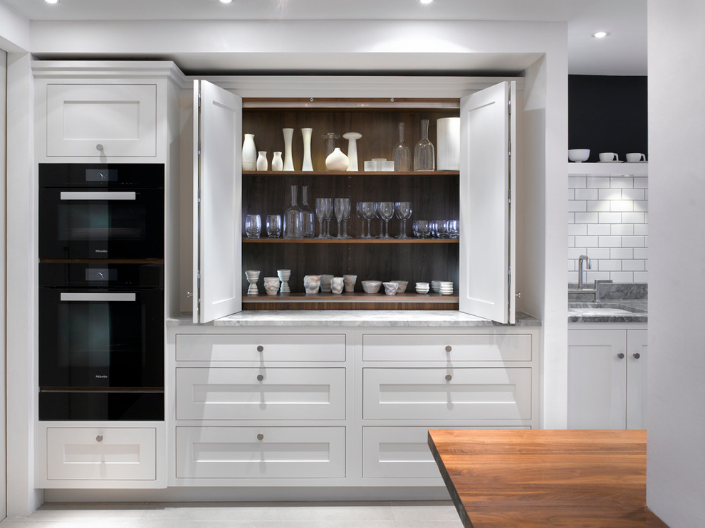 Large contemporary kitchen pantry in London with an undermount sink, recessed-panel cabinets, white cabinets, marble benchtops, white splashback, ceramic splashback and black appliances.