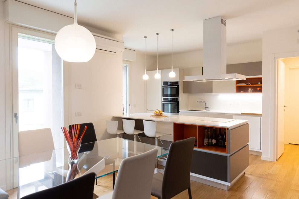 This is an example of a mid-sized contemporary galley eat-in kitchen in Milan with with island, a single-bowl sink, flat-panel cabinets, white cabinets, white splashback, white benchtop, light hardwood floors and brown floor.