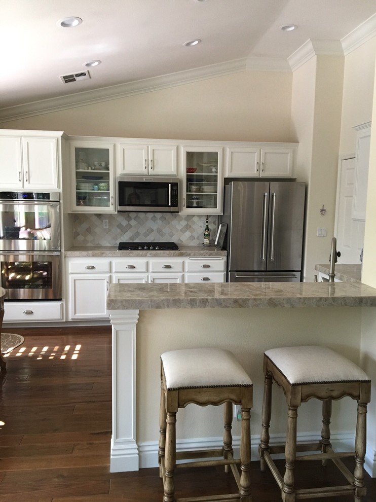 Photo of a mid-sized country u-shaped open plan kitchen in Los Angeles with an undermount sink, glass-front cabinets, white cabinets, quartzite benchtops, multi-coloured splashback, mosaic tile splashback, stainless steel appliances, dark hardwood floors and a peninsula.