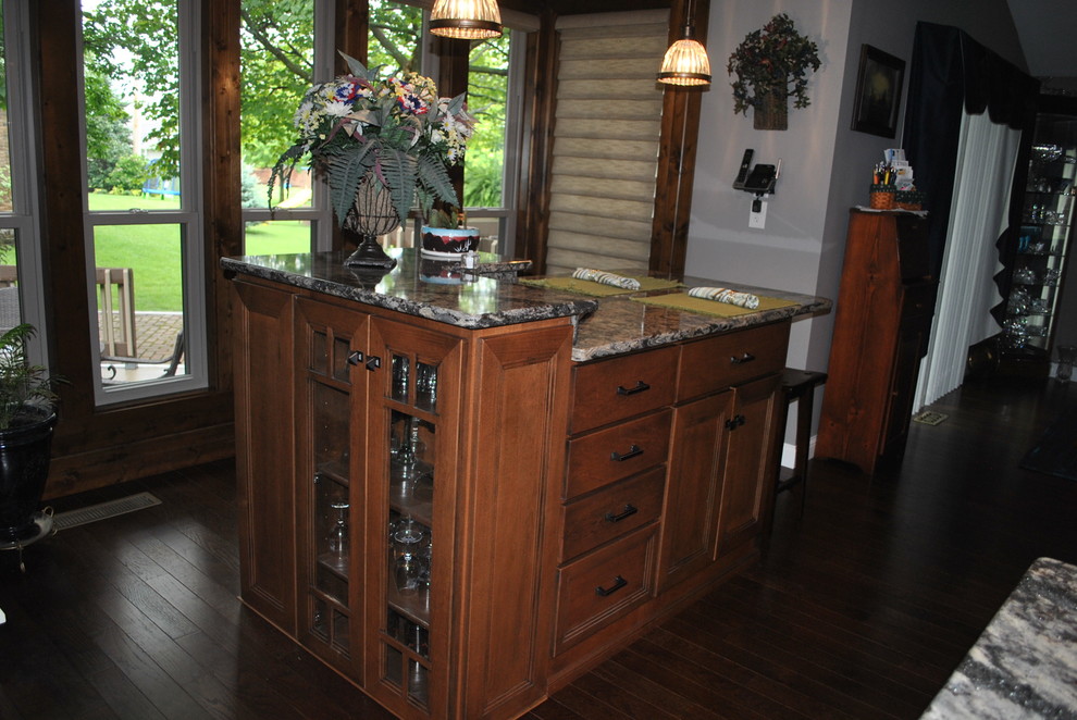 Brown floor kitchen photo with brown cabinets, beige backsplash, stainless steel appliances, an island and gray countertops
