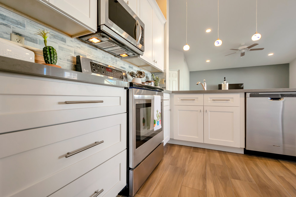 Design ideas for a mid-sized contemporary l-shaped open plan kitchen in Phoenix with an undermount sink, shaker cabinets, white cabinets, quartz benchtops, blue splashback, glass tile splashback, porcelain floors, a peninsula, brown floor and grey benchtop.