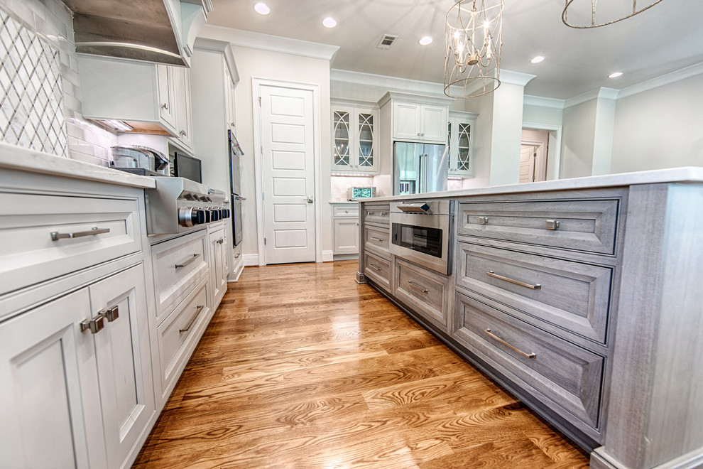 Inspiration for a large traditional u-shaped open plan kitchen in Birmingham with a farmhouse sink, beaded inset cabinets, grey cabinets, quartz benchtops, grey splashback, subway tile splashback, stainless steel appliances, medium hardwood floors, with island and brown floor.