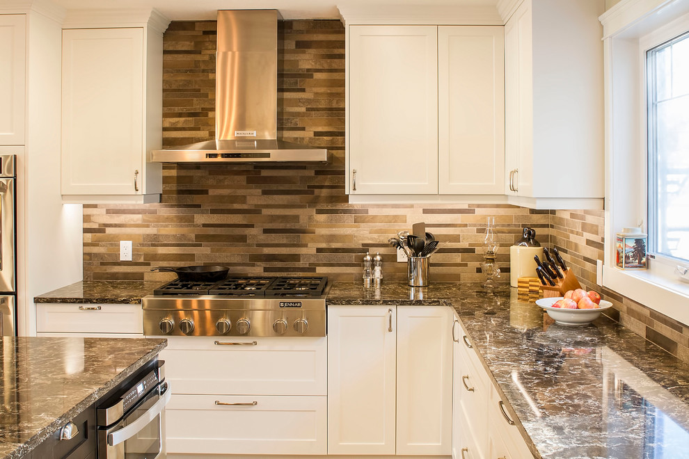 Large transitional l-shaped eat-in kitchen photo with a farmhouse sink, shaker cabinets, white cabinets, quartz countertops, brown backsplash, stone tile backsplash, stainless steel appliances and an island