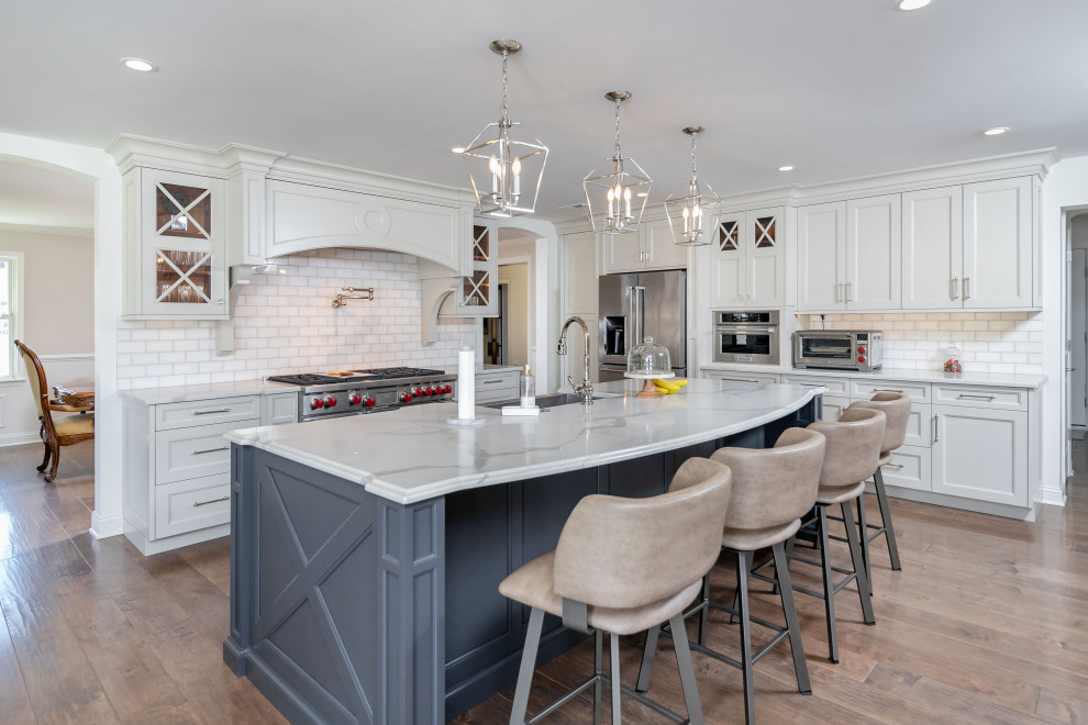 Photo of an expansive transitional l-shaped kitchen in Philadelphia with an undermount sink, shaker cabinets, white cabinets, white splashback, subway tile splashback, stainless steel appliances, medium hardwood floors, with island, beige floor and grey benchtop.