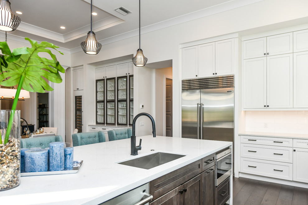 Beach style l-shaped kitchen in Tampa with an undermount sink, shaker cabinets, white cabinets, quartz benchtops, white splashback, subway tile splashback, stainless steel appliances, dark hardwood floors, with island and brown floor.