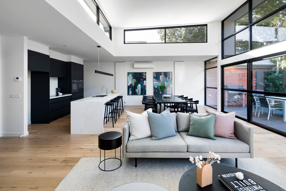 This is an example of a mid-sized modern open concept living room in Melbourne with white walls, light hardwood floors, a standard fireplace, a plaster fireplace surround, a wall-mounted tv and brown floor.