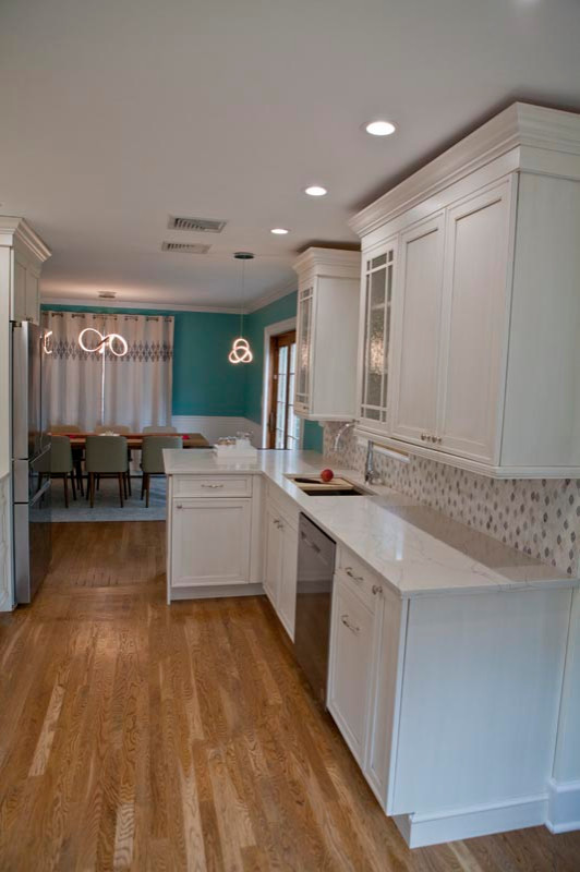 Mid-sized transitional l-shaped dark wood floor, brown floor and shiplap ceiling eat-in kitchen photo in New York with an integrated sink, shaker cabinets, white cabinets, quartz countertops, gray backsplash, ceramic backsplash, stainless steel appliances, an island and white countertops