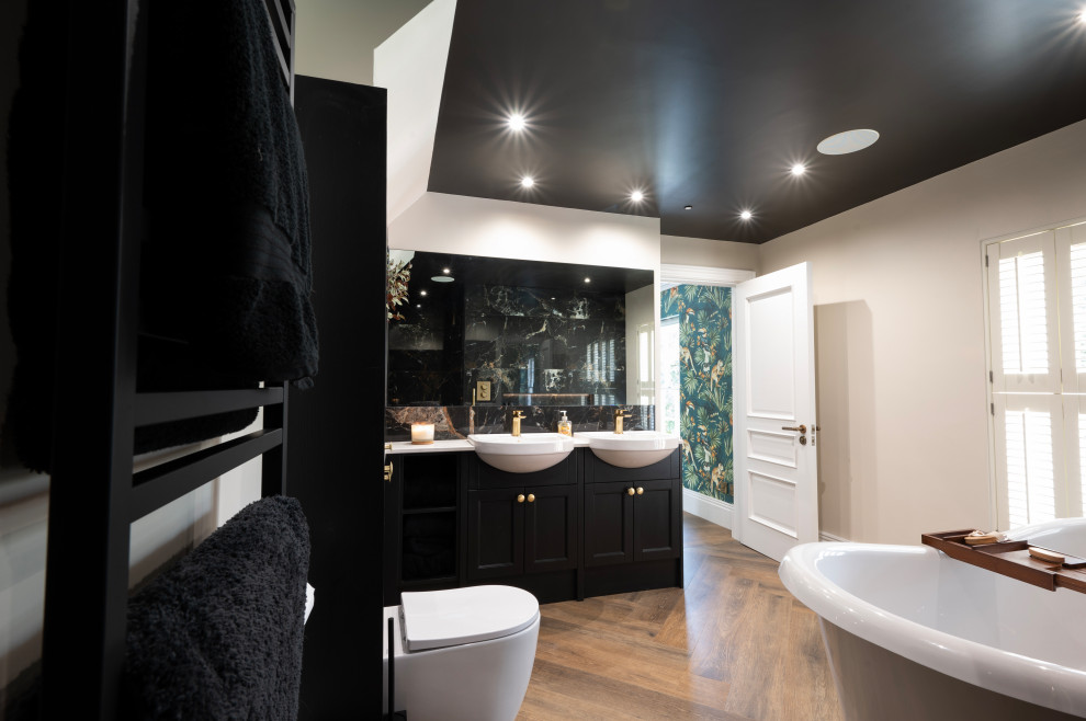 Пример оригинального дизайна: главная ванная комната среднего размера с фасадами с утопленной филенкой, черными фасадами, отдельно стоящей ванной, открытым душем, унитазом-моноблоком, керамической плиткой, черными стенами, полом из винила, монолитной раковиной, коричневым полом, открытым душем, белой столешницей, акцентной стеной, тумбой под две раковины и встроенной тумбой