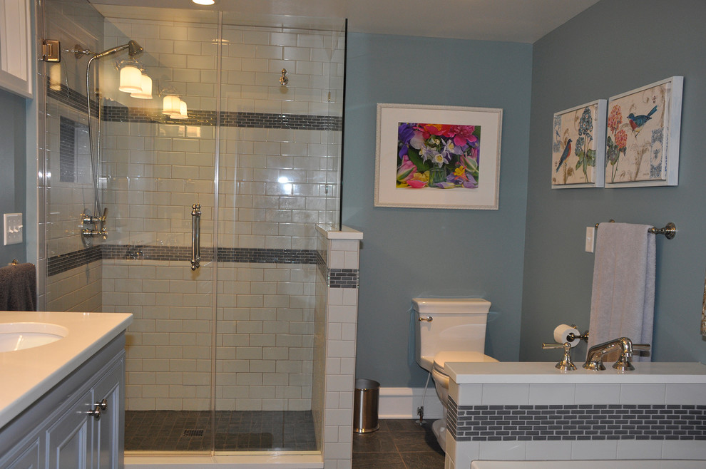 Inspiration for a mid-sized arts and crafts 3/4 bathroom in Milwaukee with recessed-panel cabinets, white cabinets, a corner shower, a two-piece toilet, gray tile, white tile, subway tile, grey walls, ceramic floors, an undermount sink, solid surface benchtops, grey floor and a hinged shower door.