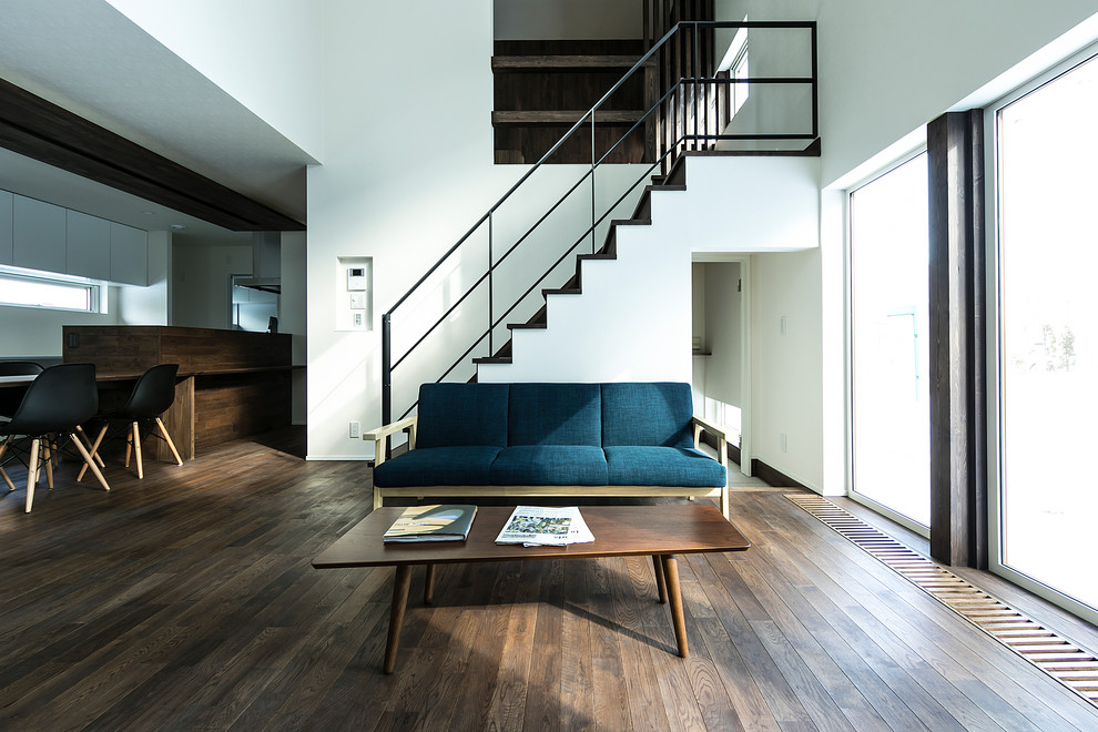 This is an example of an asian open concept living room in Sapporo with white walls, dark hardwood floors and brown floor.