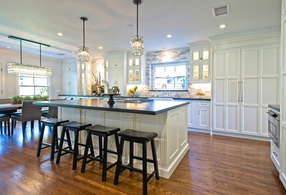 Design ideas for a large arts and crafts galley eat-in kitchen in Orange County with a farmhouse sink, shaker cabinets, white cabinets, quartz benchtops, grey splashback, marble splashback, stainless steel appliances, medium hardwood floors, with island, brown floor and black benchtop.