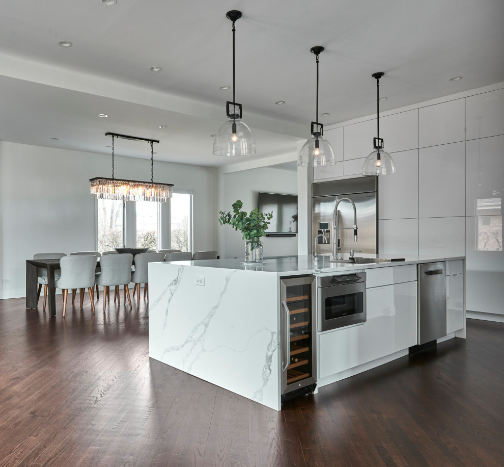 Inspiration for a large transitional single-wall eat-in kitchen in Chicago with a drop-in sink, flat-panel cabinets, white cabinets, quartzite benchtops, white splashback, marble splashback, stainless steel appliances, dark hardwood floors, with island, brown floor and white benchtop.