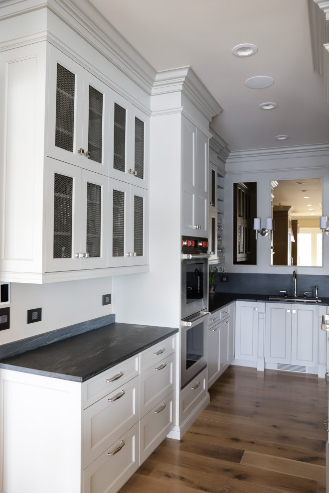 This is an example of a mid-sized transitional u-shaped open plan kitchen in New York with an undermount sink, shaker cabinets, beige cabinets, grey splashback, stainless steel appliances, dark hardwood floors, with island, black floor and white benchtop.