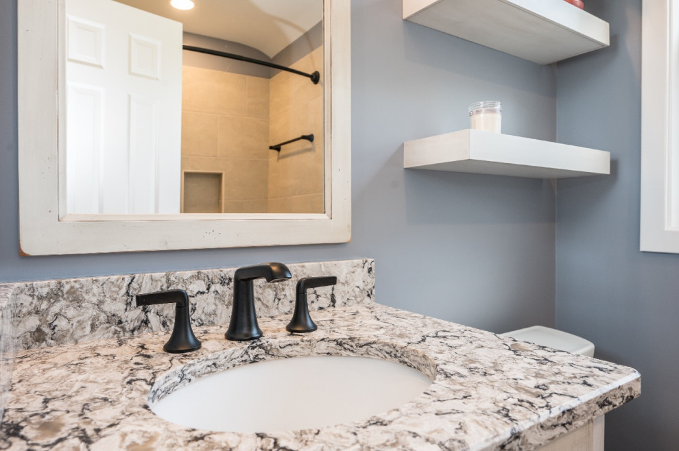 This is an example of a small country 3/4 bathroom in DC Metro with shaker cabinets, distressed cabinets, a shower/bathtub combo, a two-piece toilet, grey walls, ceramic floors, an undermount sink, granite benchtops, brown floor, multi-coloured benchtops, a single vanity and a built-in vanity.