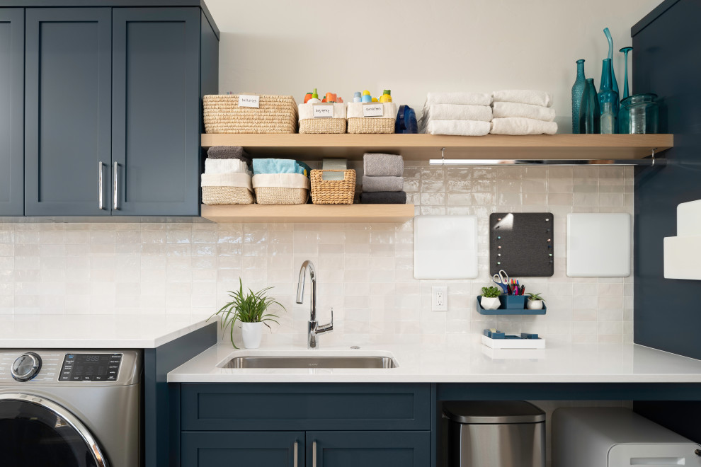 This is an example of a modern utility room in Denver with an undermount sink, shaker cabinets, blue cabinets, quartz benchtops, white splashback, ceramic splashback, white walls, porcelain floors, a side-by-side washer and dryer and white benchtop.