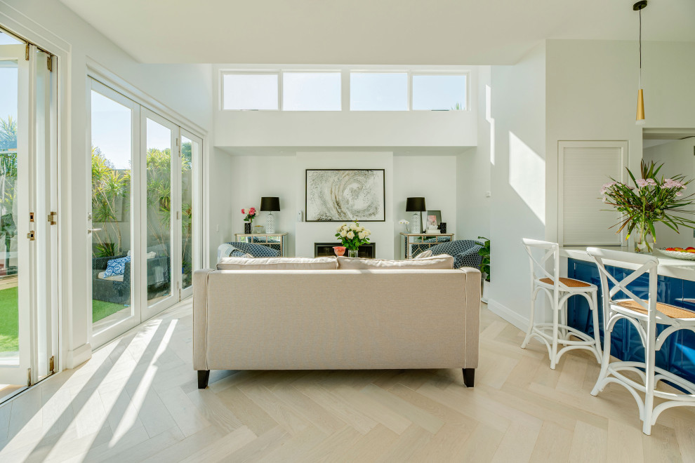 Photo of a mid-sized contemporary open concept family room in Sydney with white walls, light hardwood floors, a wall-mounted tv and beige floor.