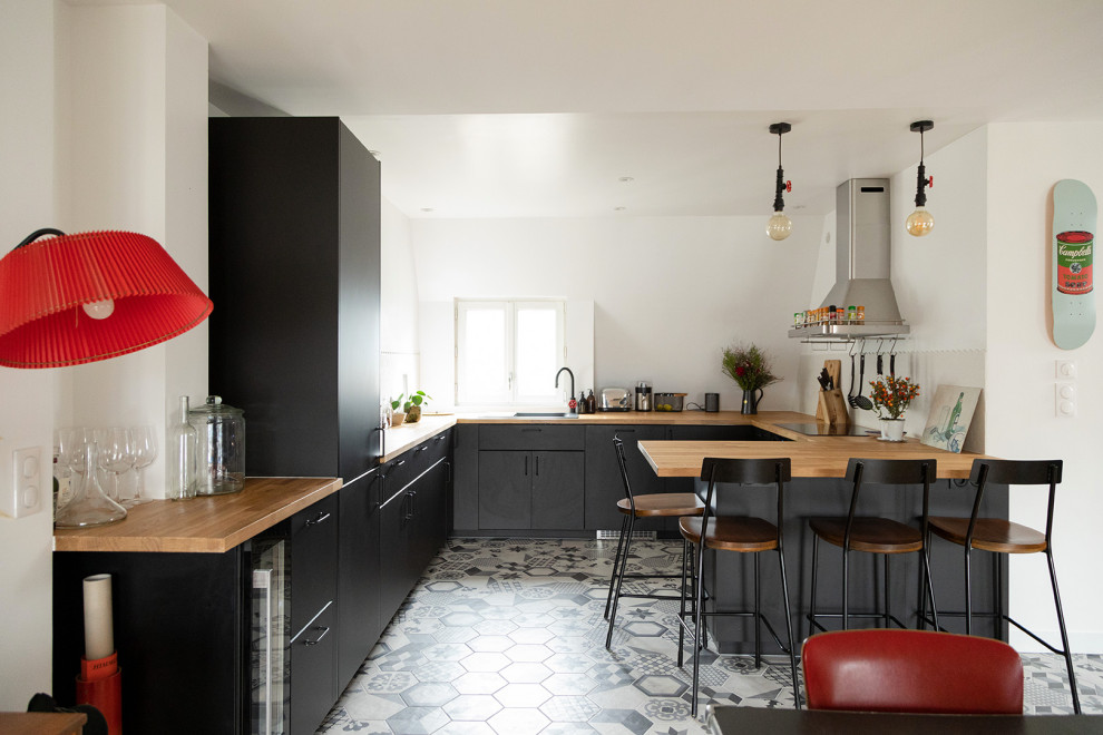 Inspiration for a mid-sized contemporary u-shaped open plan kitchen in Paris with a drop-in sink, flat-panel cabinets, black cabinets, wood benchtops, white splashback, mosaic tile splashback, panelled appliances, cement tiles, with island, black floor and brown benchtop.