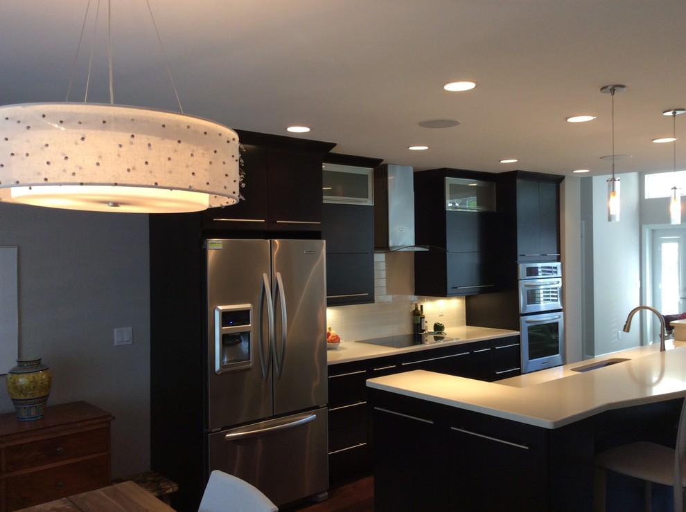 Large transitional galley eat-in kitchen photo in Chicago with an undermount sink, flat-panel cabinets, black cabinets, solid surface countertops, white backsplash, glass tile backsplash, stainless steel appliances and an island