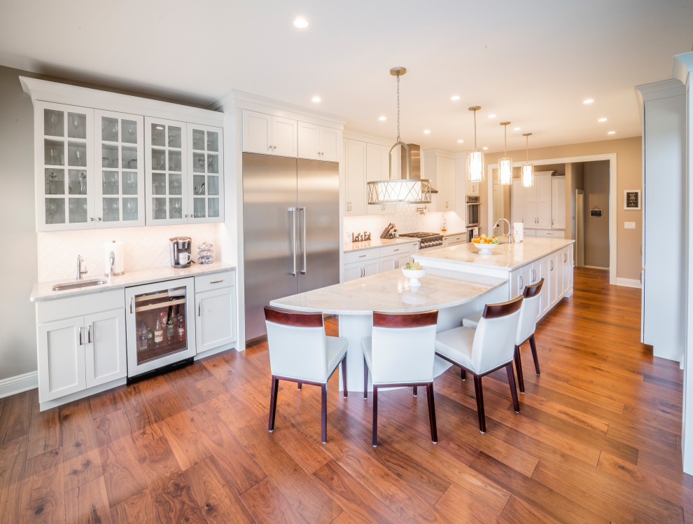 Large transitional u-shaped medium tone wood floor and brown floor kitchen pantry photo with an undermount sink, shaker cabinets, white cabinets, granite countertops, white backsplash, ceramic backsplash, stainless steel appliances, an island and white countertops