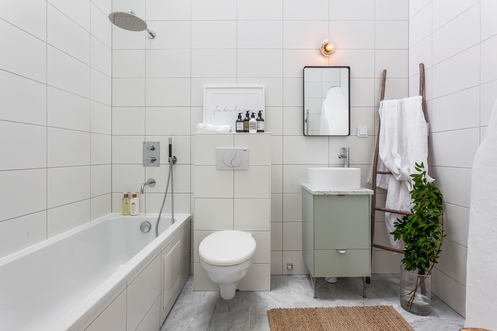 This is an example of a mid-sized scandinavian master bathroom in Stockholm with flat-panel cabinets, green cabinets, a drop-in tub, a shower/bathtub combo, a wall-mount toilet, white tile, a vessel sink, white walls, marble floors and an open shower.