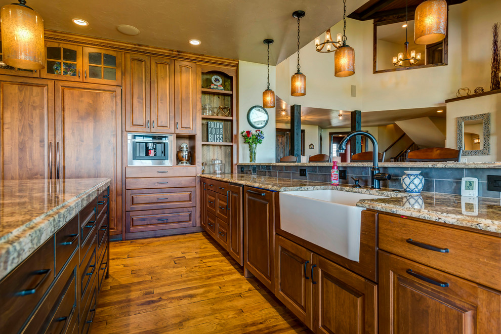 Large arts and crafts open plan kitchen in Denver with a farmhouse sink, raised-panel cabinets, medium wood cabinets, granite benchtops, grey splashback, subway tile splashback, panelled appliances, medium hardwood floors, with island and brown floor.