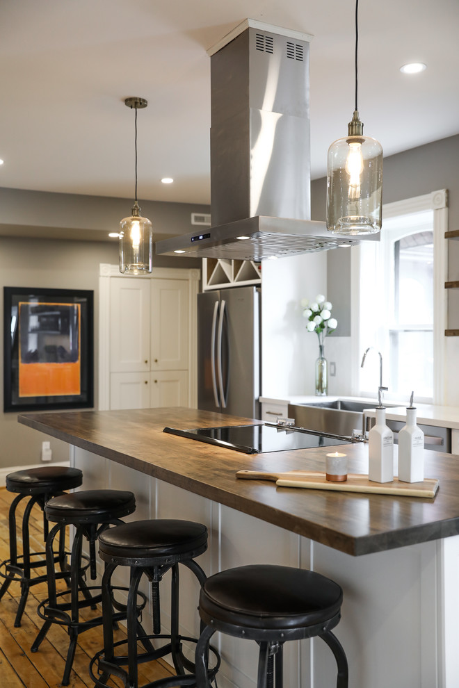 Example of a mid-sized transitional single-wall medium tone wood floor and brown floor eat-in kitchen design with a farmhouse sink, shaker cabinets, white cabinets, white backsplash, stainless steel appliances, an island and white countertops