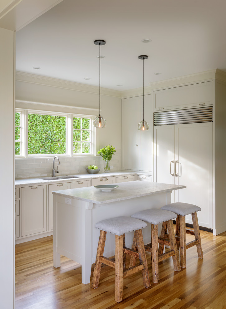 Inspiration for a mid-sized transitional u-shaped light wood floor kitchen remodel in Seattle with an undermount sink, shaker cabinets, white cabinets, quartzite countertops, blue backsplash, ceramic backsplash, paneled appliances and an island