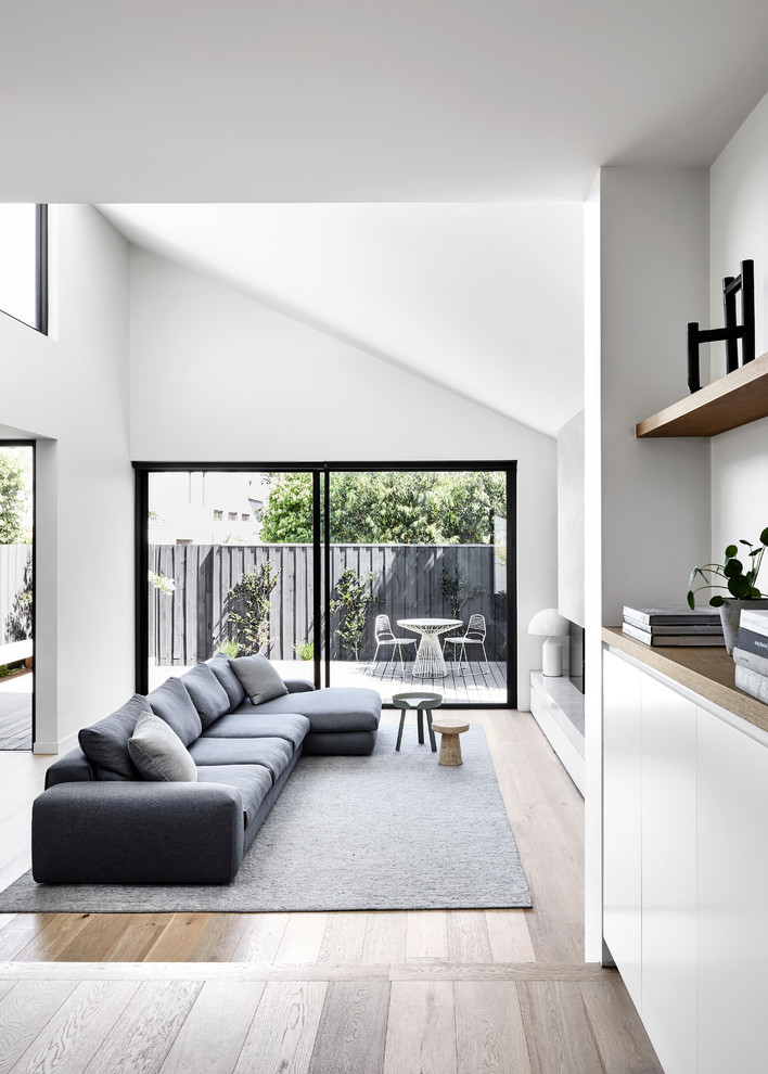 Inspiration for a mid-sized contemporary open concept living room in Melbourne with white walls, light hardwood floors, a standard fireplace, a metal fireplace surround, a wall-mounted tv and brown floor.