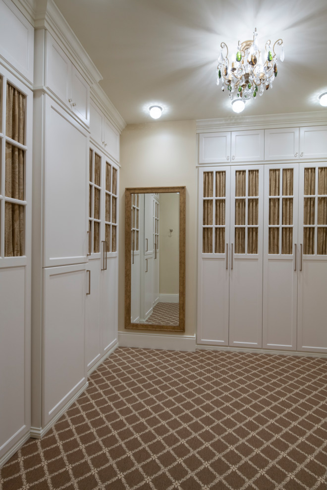 Пример оригинального дизайна: большая гардеробная комната в классическом стиле с фасадами с утопленной филенкой, белыми фасадами, ковровым покрытием и коричневым полом для женщин