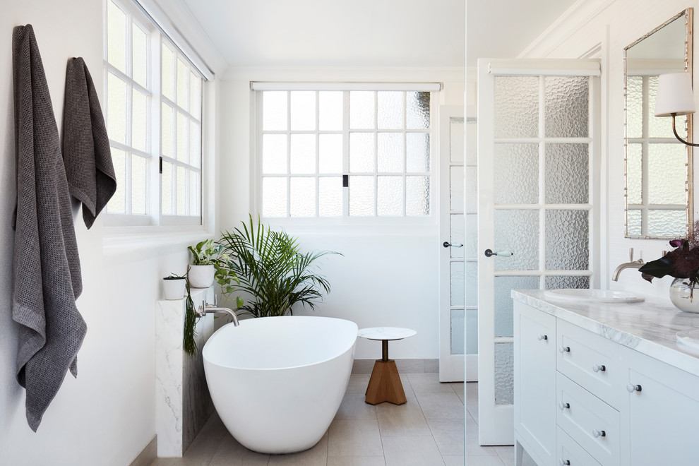 Design ideas for a large transitional master bathroom in Sydney with shaker cabinets, white cabinets, a freestanding tub, an open shower, a wall-mount toilet, white tile, marble, white walls, porcelain floors, a drop-in sink, marble benchtops, grey floor, an open shower and white benchtops.