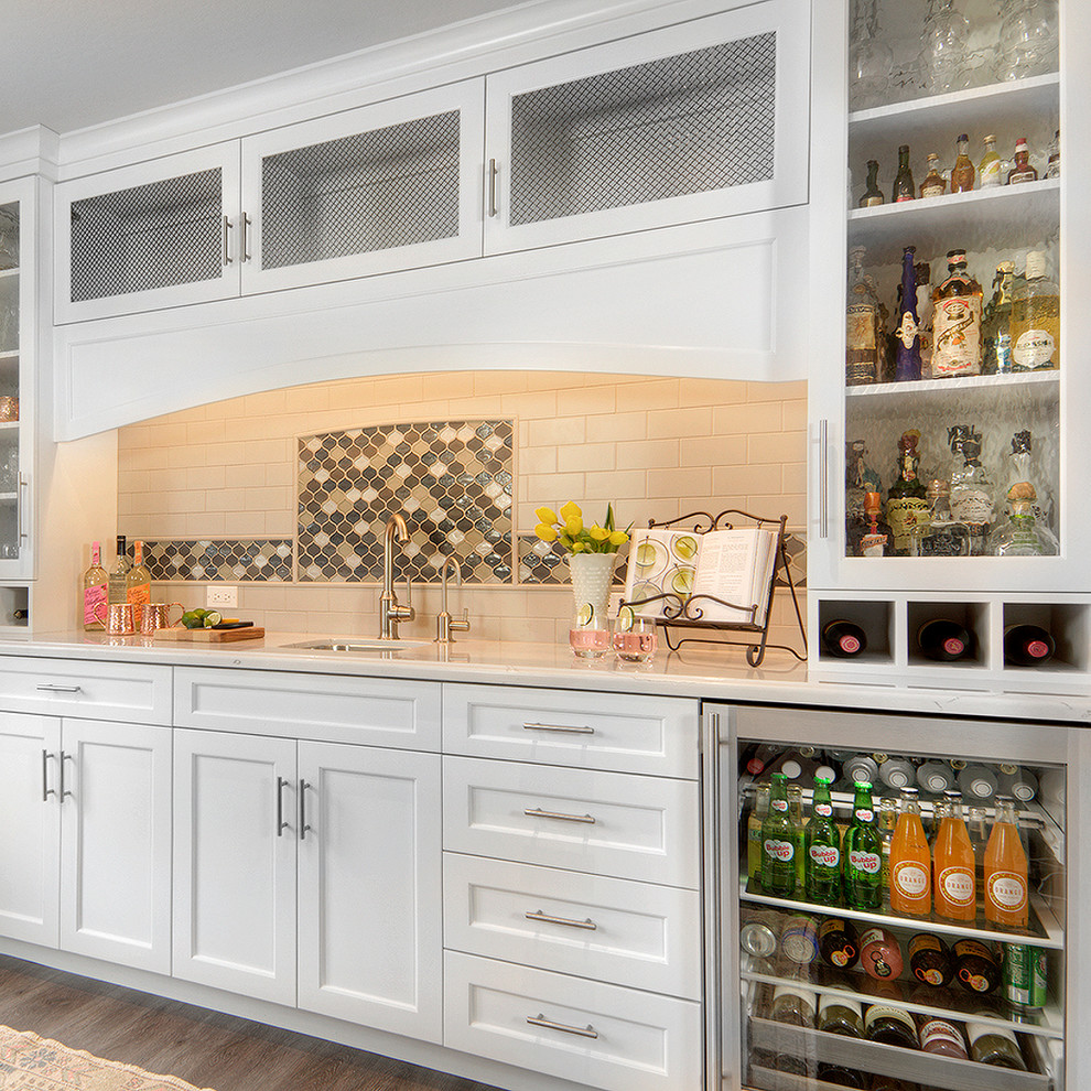 Photo of a mid-sized transitional galley wet bar in San Francisco with an undermount sink, shaker cabinets, white cabinets, quartz benchtops, multi-coloured splashback, mosaic tile splashback, vinyl floors, brown floor and white benchtop.