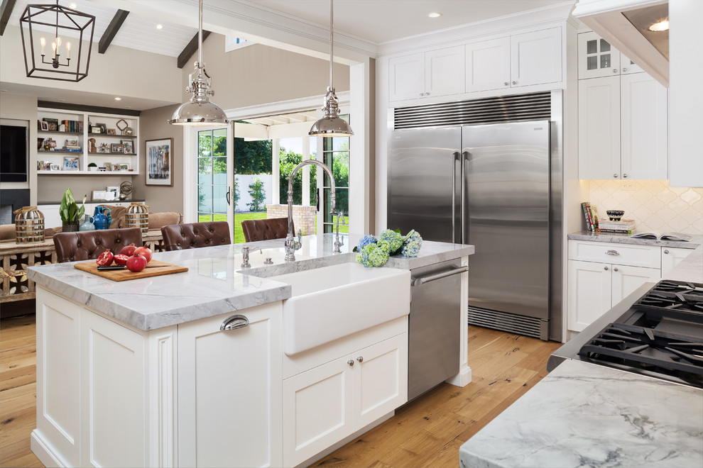 Large transitional u-shaped separate kitchen in Phoenix with a farmhouse sink, shaker cabinets, white cabinets, onyx benchtops, white splashback, ceramic splashback, stainless steel appliances, light hardwood floors, with island and brown floor.