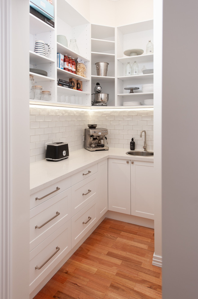 Inspiration for an expansive traditional galley kitchen pantry in Melbourne with an undermount sink, recessed-panel cabinets, white cabinets, quartz benchtops, white splashback, porcelain splashback, stainless steel appliances, medium hardwood floors, with island and white benchtop.