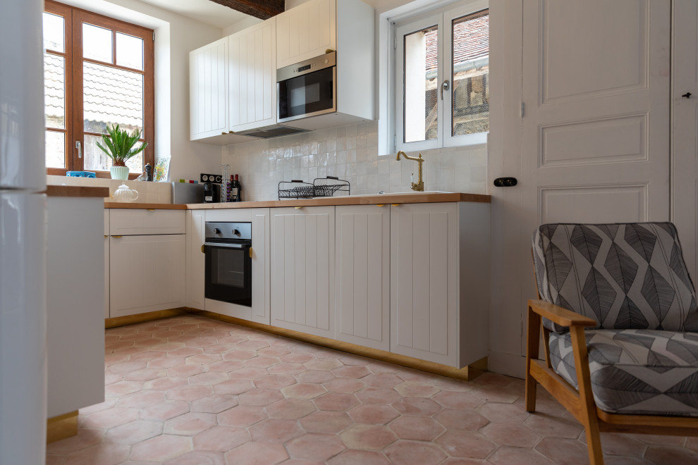 This is an example of a medium sized rural u-shaped open plan kitchen in Le Havre with a submerged sink, beaded cabinets, white cabinets, wood worktops, white splashback, integrated appliances, terracotta flooring, no island, pink floors, beige worktops and exposed beams.