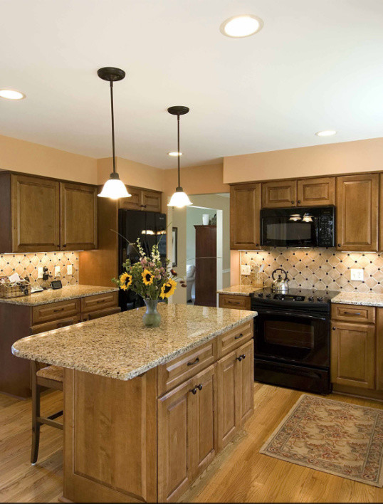 Inspiration for a mid-sized transitional l-shaped light wood floor eat-in kitchen remodel with raised-panel cabinets, medium tone wood cabinets, granite countertops, beige backsplash, black appliances and an island