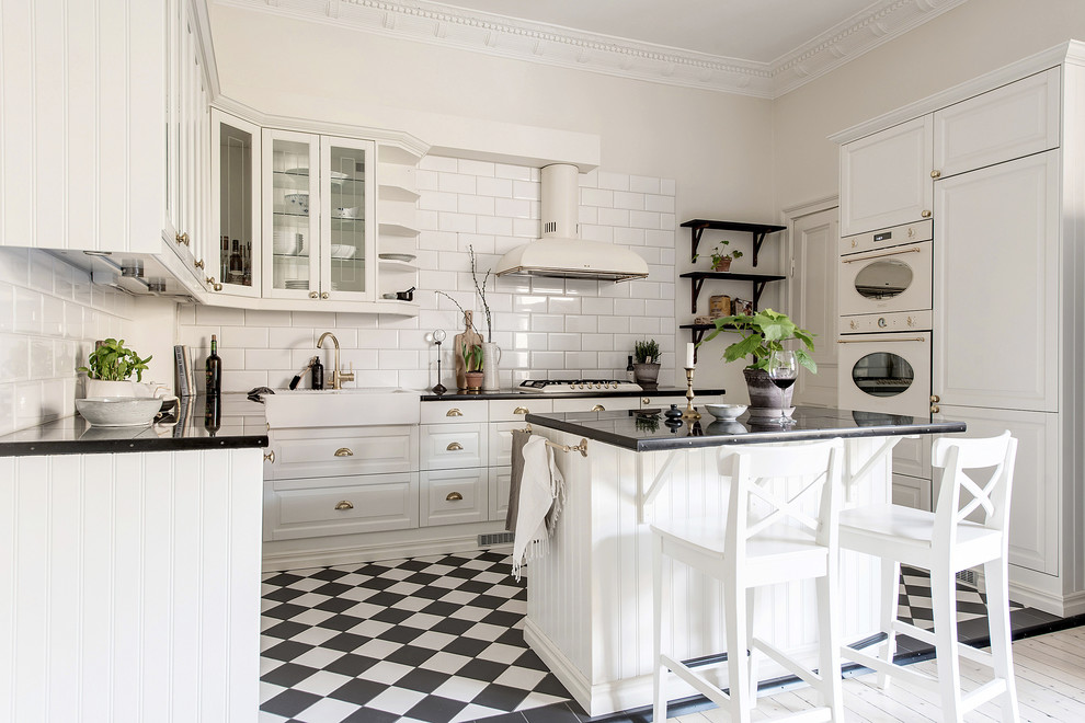 Design ideas for a mid-sized scandinavian l-shaped eat-in kitchen in Gothenburg with a double-bowl sink, glass-front cabinets, white cabinets, white splashback, with island and multi-coloured floor.