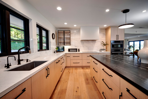 Modern kitchen with light wood cabinets, black hardware, white countertops, black island top, wide-plank wood floors