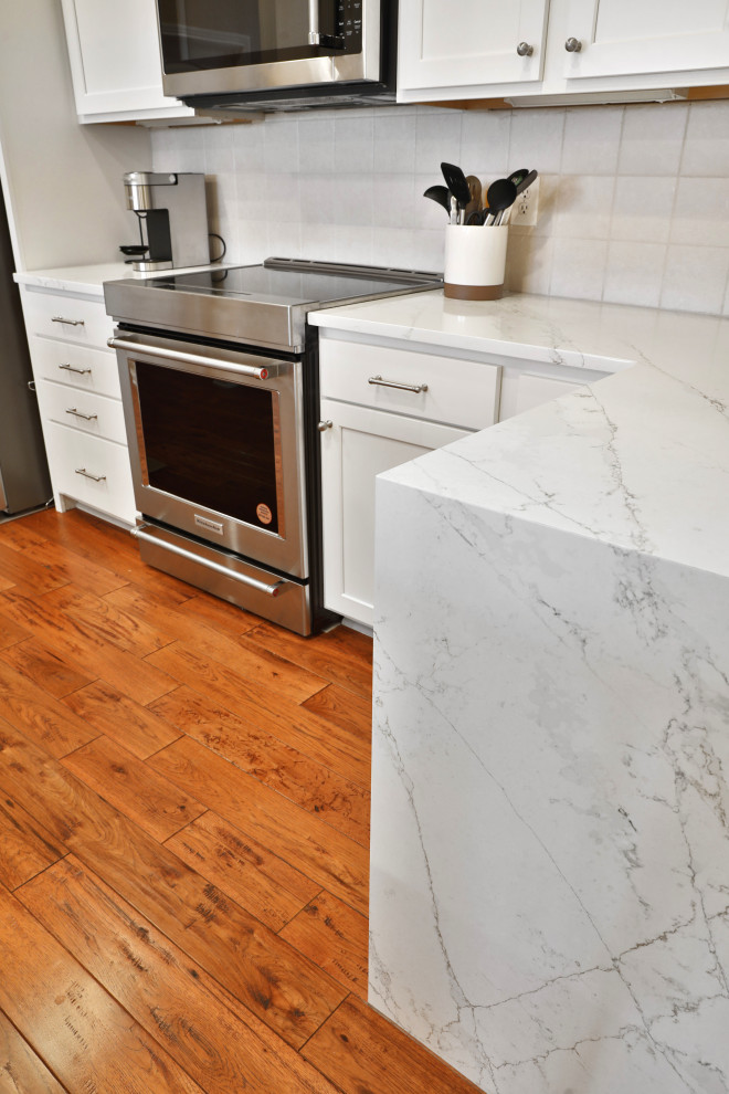 Mid-sized transitional galley medium tone wood floor and brown floor enclosed kitchen photo in Columbus with a single-bowl sink, shaker cabinets, white cabinets, quartz countertops, white backsplash, ceramic backsplash, stainless steel appliances, no island and white countertops
