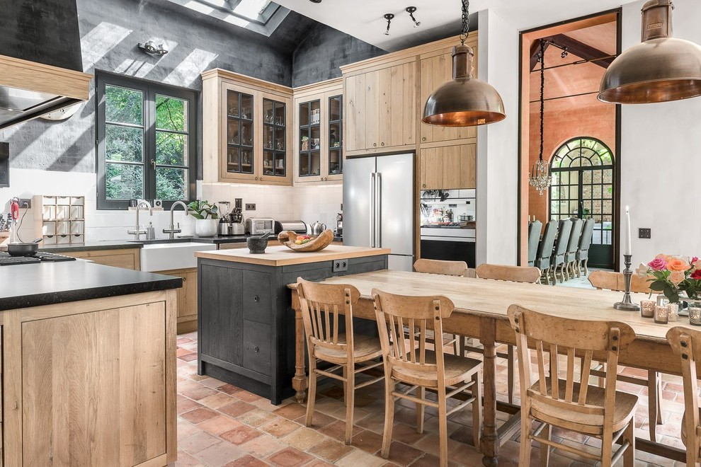 Inspiration for a country u-shaped eat-in kitchen in Marseille with a farmhouse sink, glass-front cabinets, light wood cabinets, white splashback, stainless steel appliances, terra-cotta floors, with island and orange floor.