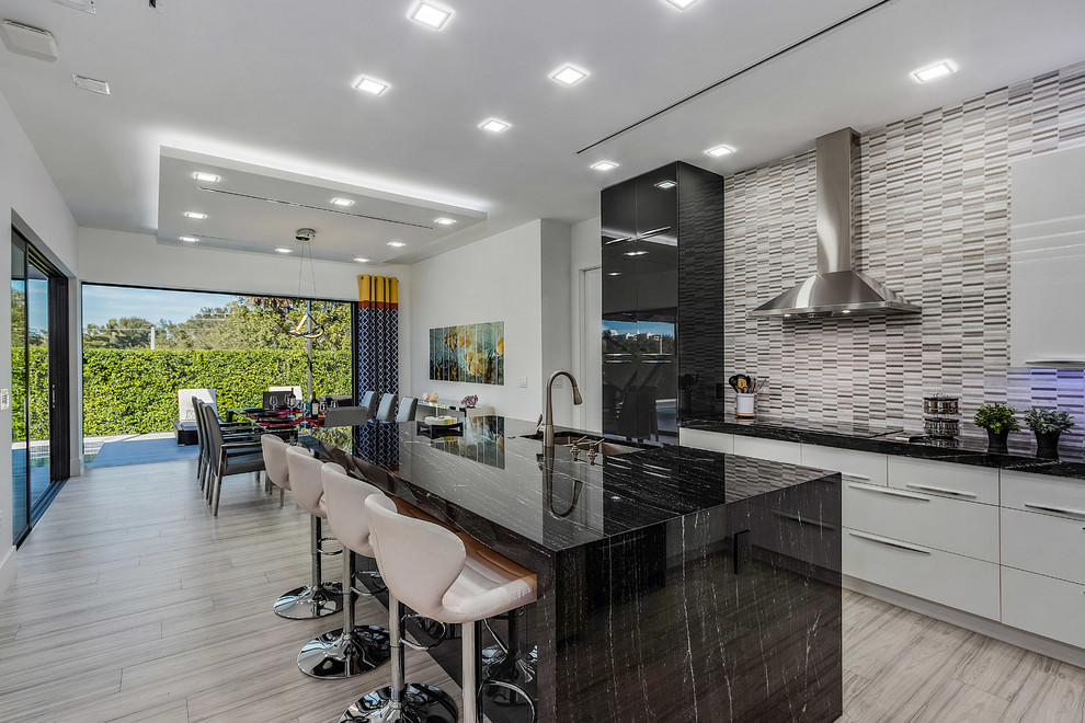 Inspiration for a contemporary eat-in kitchen in Miami with an undermount sink, flat-panel cabinets, multi-coloured splashback, matchstick tile splashback, black appliances, with island, beige floor and black benchtop.