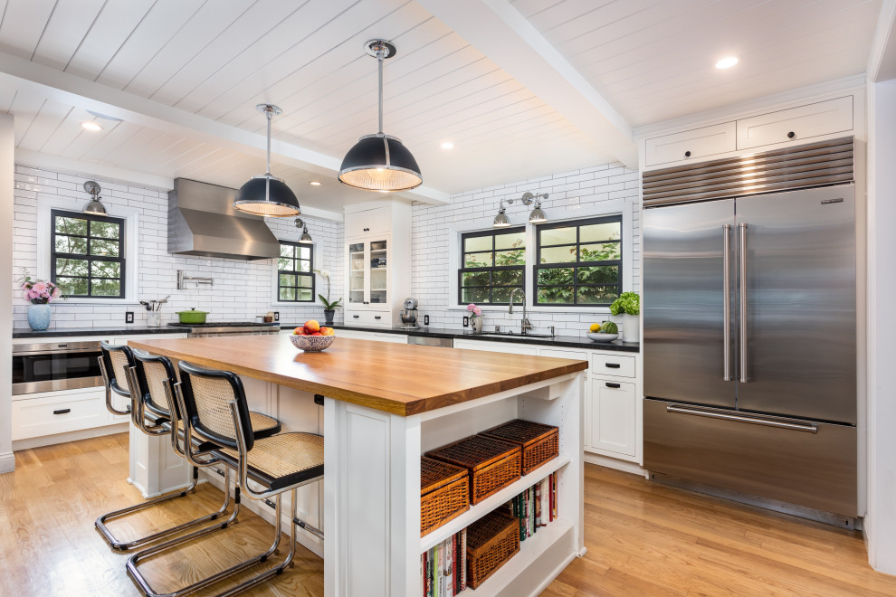 This is an example of a mid-sized country u-shaped eat-in kitchen in Los Angeles with an undermount sink, shaker cabinets, white cabinets, wood benchtops, white splashback, subway tile splashback, stainless steel appliances, light hardwood floors, with island, brown floor, brown benchtop and timber.