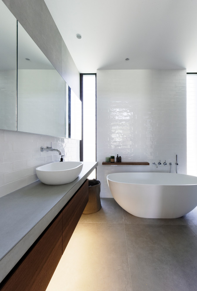 Inspiration for a mid-sized contemporary master bathroom in Central Coast with dark wood cabinets, a freestanding tub, an open shower, a wall-mount toilet, subway tile, white walls, porcelain floors, a console sink, concrete benchtops, grey floor, an open shower, grey benchtops and flat-panel cabinets.